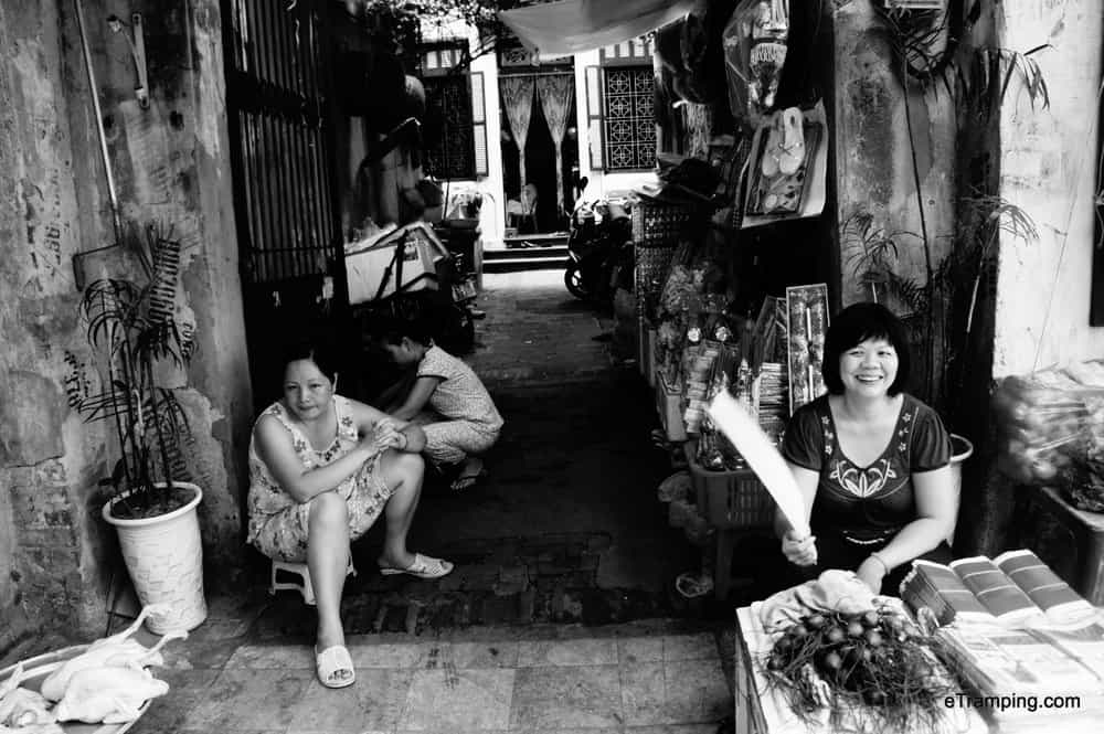 A sidewalk lined with various shops and ladies selling wares to locals and tourists.