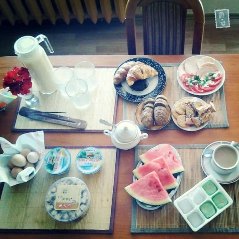 Breakfast table with croissants, milk, ham, cookies, fruits