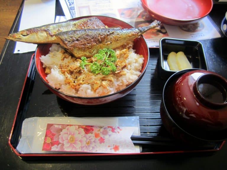 a bowl of miso soup, a bed of rice, fish, and pickled radishes. 