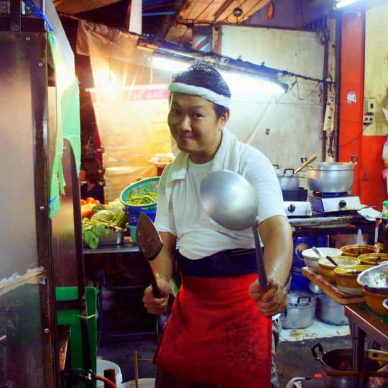 A Thai cook is holding cooking equipment 
