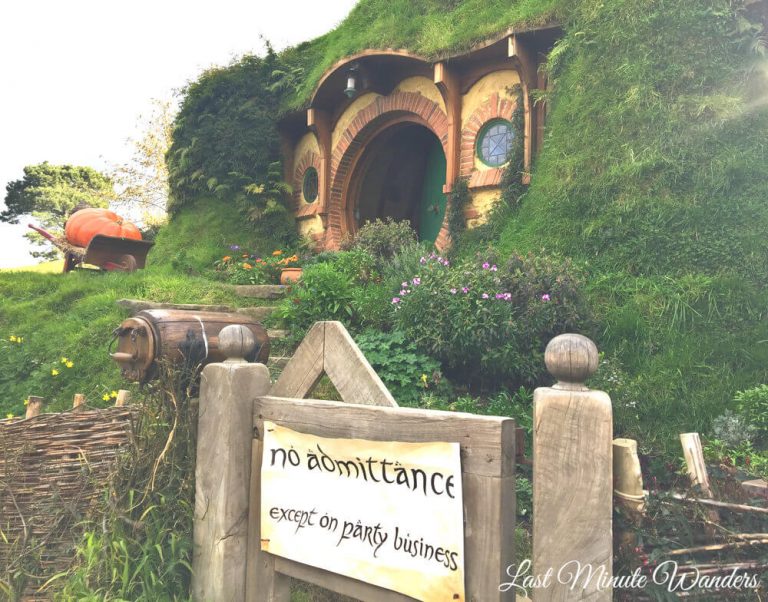 A round door in the side of a grassy hill and a garden gate with a paper sign stating "no admittance except on party business".