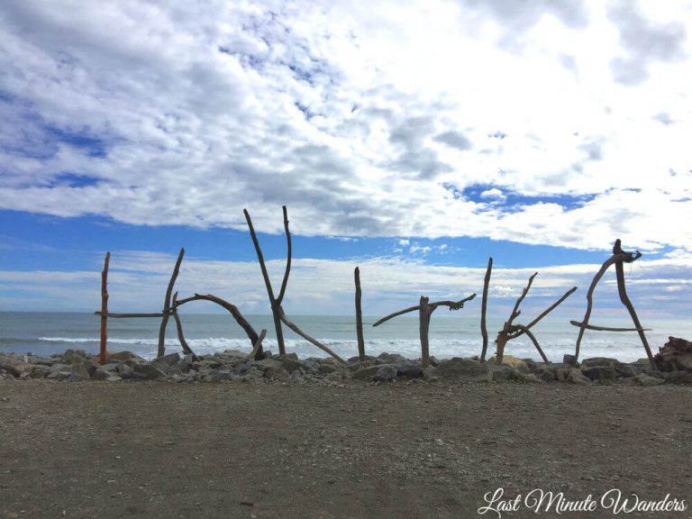 View out to sea from beach with large driftwood letters spelling out "Hokitika".