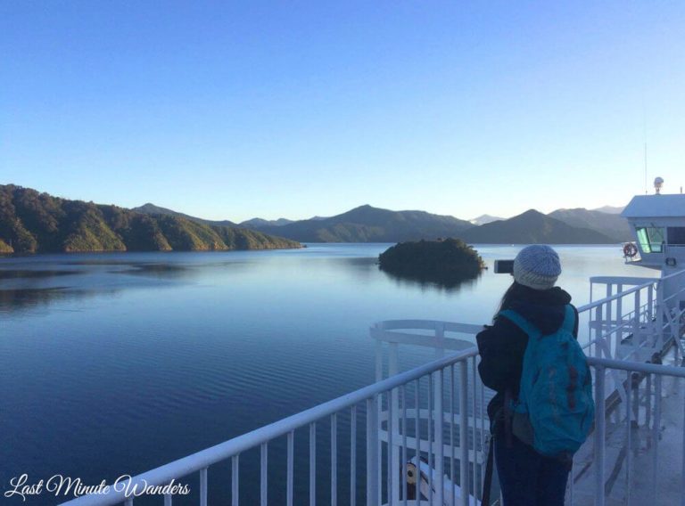 Woman on deck of ferry taking photos of the mountains and water.