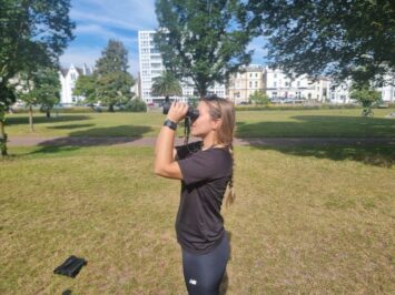 woman looking through binoculars in grassy field outdoor shot
